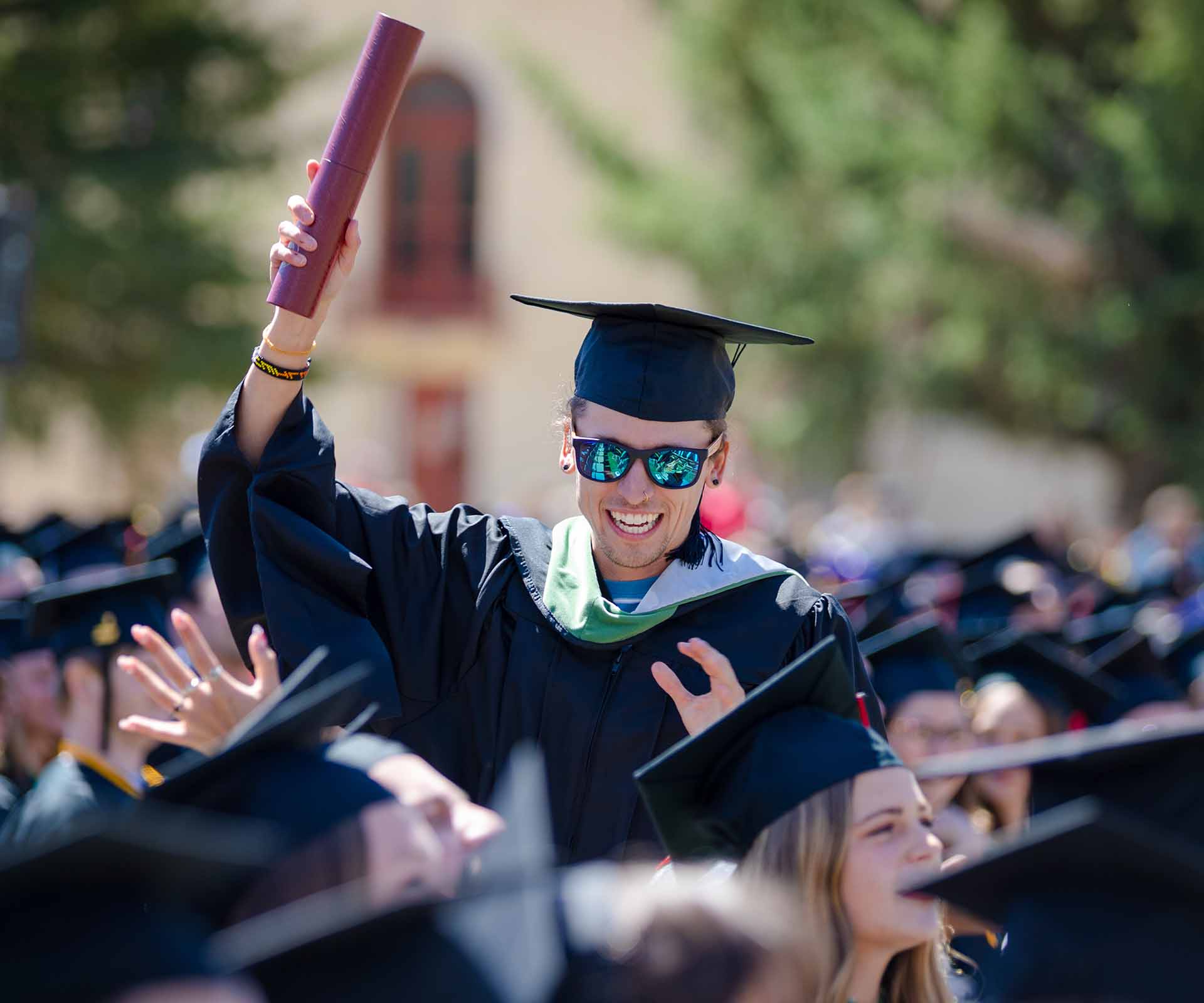 2023 Commencement Student holds diploma in the air as celebration.